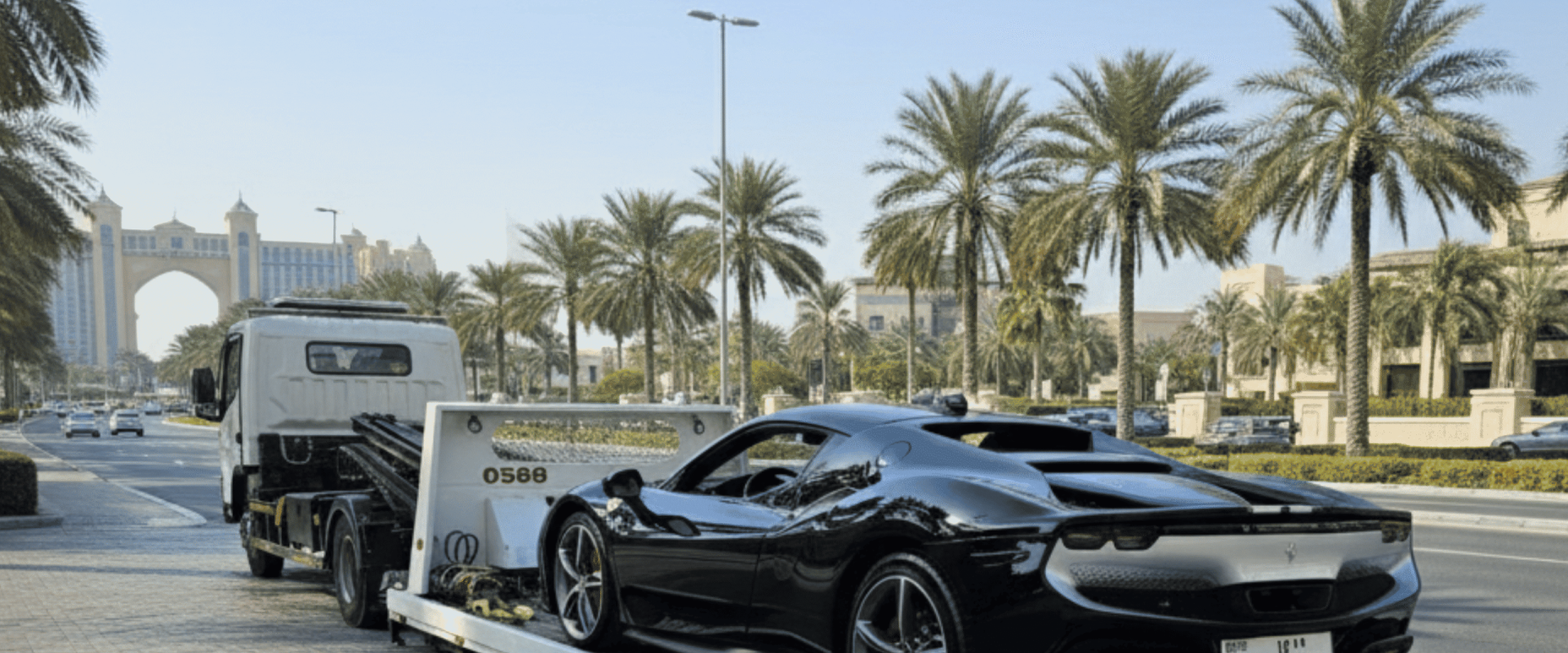 A Car image for "car recovery in Dubai" shows a white recovery truck carefully picking up a sleek, black breakdown sports car on the streets of Palm Jumeirah. The scene highlights "breakdown assistance Dubai" and "sports car towing Dubai" with the iconic Atlantis, The Palm resort visible in the background, making it ideal for "vehicle recovery services Dubai" and "roadside assistance Dubai.